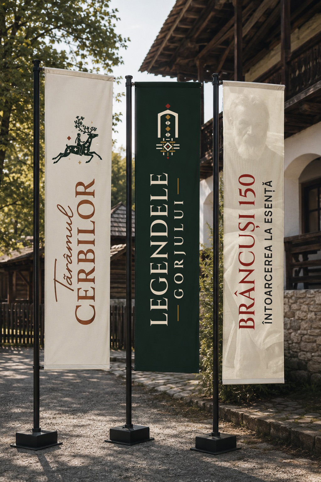 Three vertical flags in front of a traditional wooden house: Tărâmul Cerbilor, Legendele Gorjului on dark green, and the edition theme, “Brâncuși 150 · Întoarcerea la esență”
