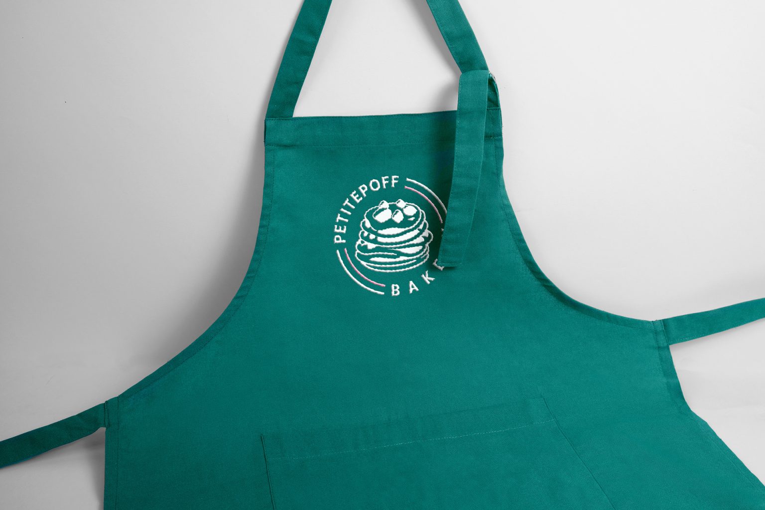 Teal apron with the white PetitePoff Bakery logo on the chest