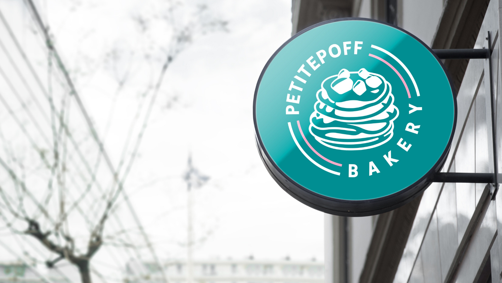 Round sign with the PetitePoff Bakery logo, bracket-mounted on the shopfront