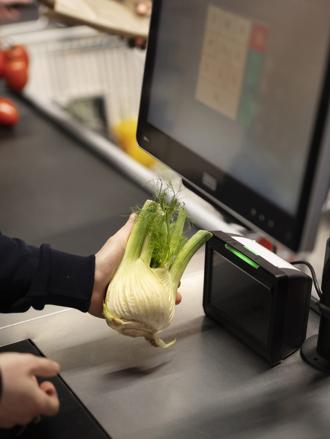 A shopper scans a vegetable at a self-scan checkout with a touchscreen and a barcode reader